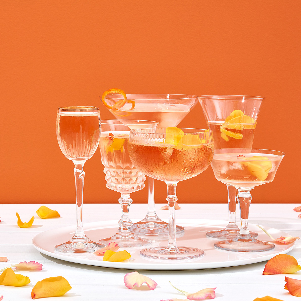 Coupes et flûtes de champagne rosé et pétales de roses sur fond orange